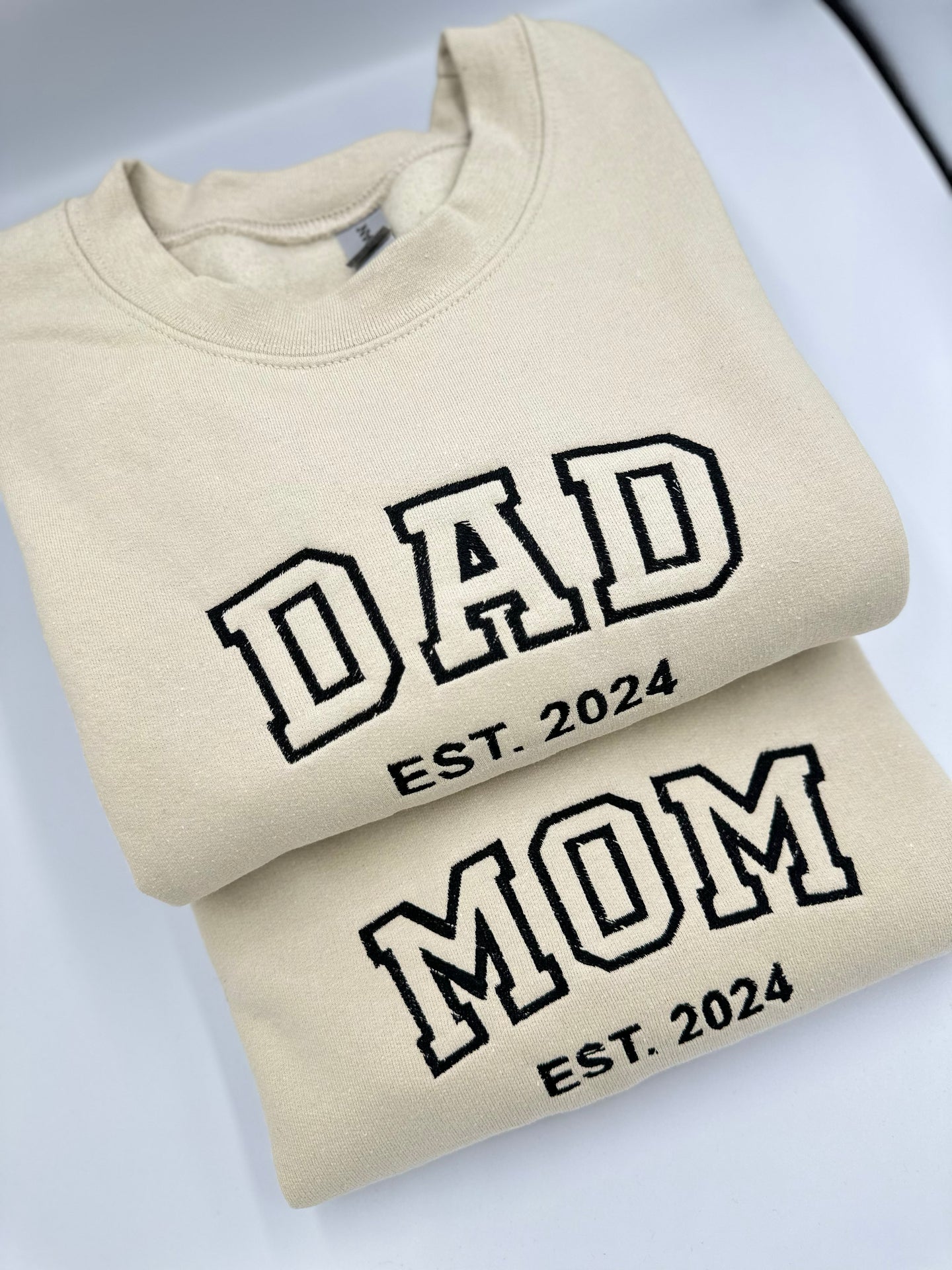 a pair of sweatshirts that say dad est 2024 and mom est 2024