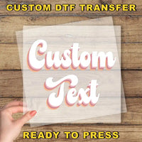 The image is a promotional image for a custom DTF (Digital Transfer Factory) transfer service. It features a hand holding a clear sheet with the text "Custom Text" written on it, placed on a wooden background. The text "Ready to Press" is also visible, indicating that the image is ready for use.