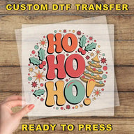A hand is holding a clear sheet with a colorful, festive design featuring the text "HO HO HO!" surrounded by various holiday-themed elements such as stars, holly leaves, and a Christmas tree.