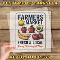 The image is a poster for a farmers market, featuring various fruits and vegetables such as bananas, apples, and avocados. The poster is displayed on a wooden surface, and there is a hand holding it up, suggesting that it is ready to be printed or displayed.