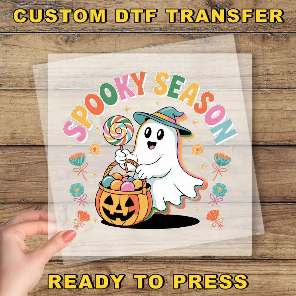 A hand is holding a clear sheet with a Halloween-themed graphic design featuring a ghost character holding a lollipop and a pumpkin.
