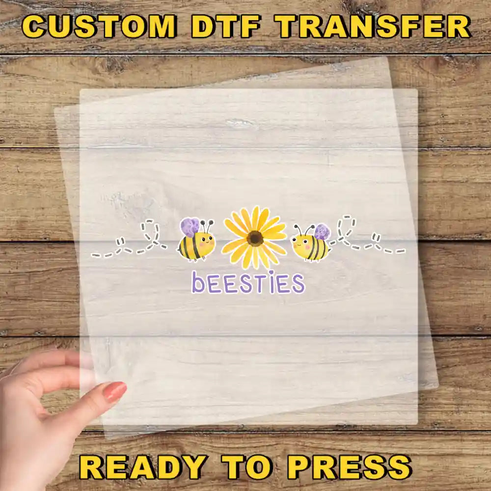 A hand is holding a transparent sheet with a design featuring a yellow flower and two bees, along with the text "beesites" written below the flower.