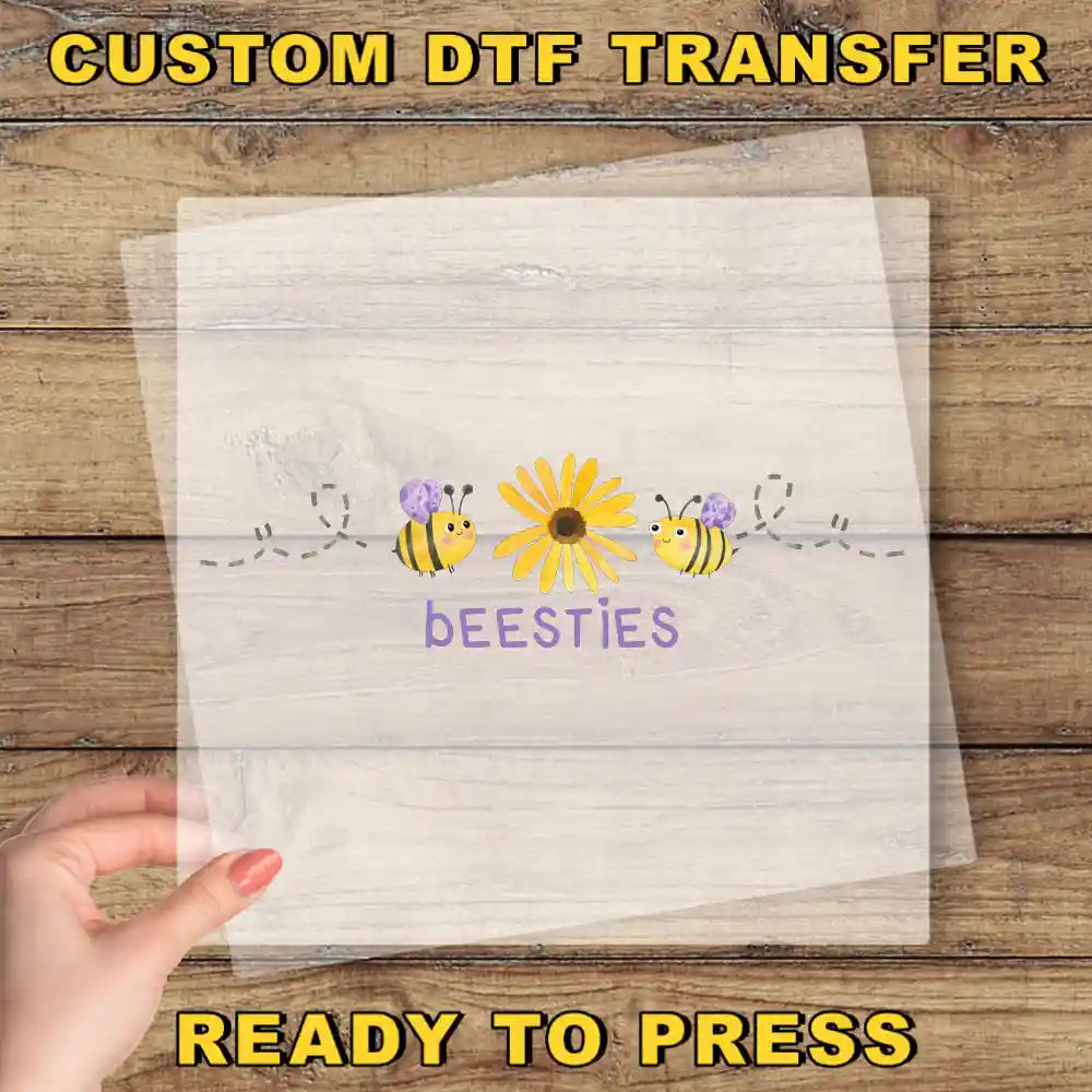 A hand is holding a transparent sheet with a design featuring a yellow flower and two bees, with the word "bees" written below the flower.