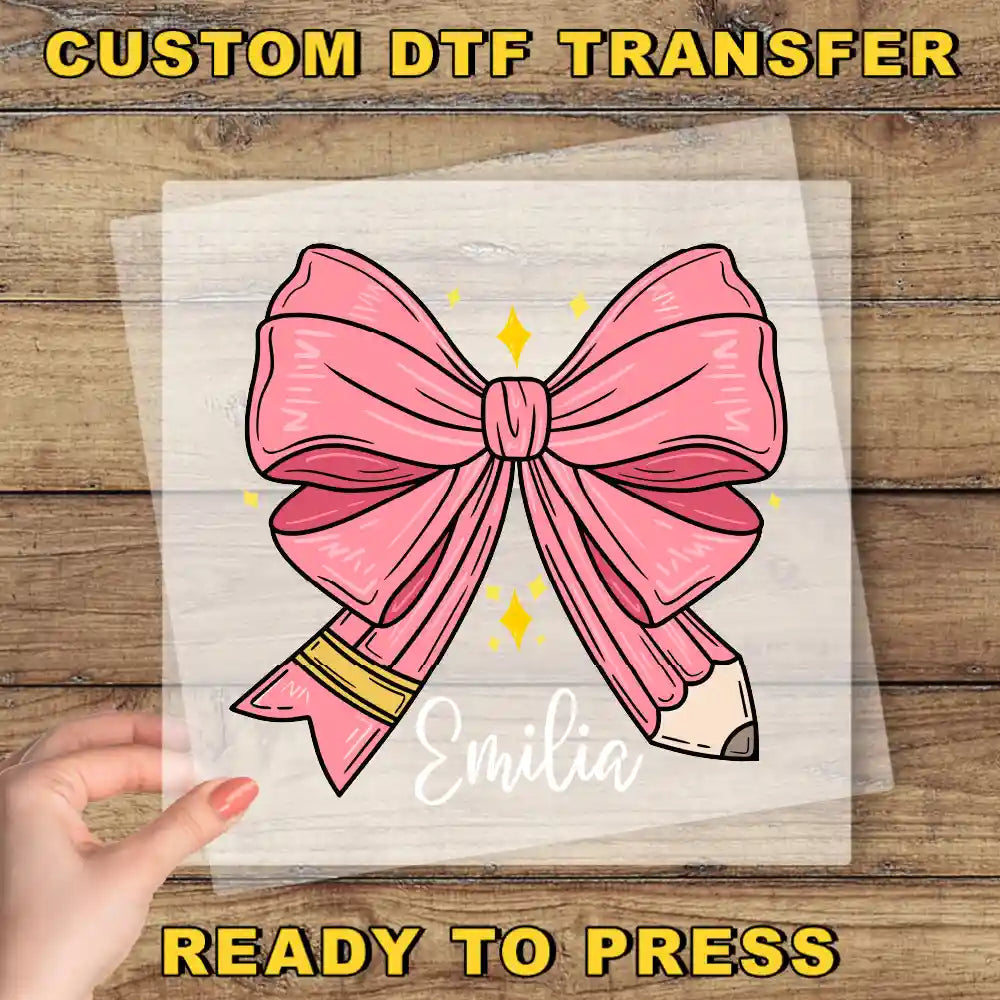 a hand holding a transparent sheet with a pink bow and a pencil, with the name "Emilia" written on it.