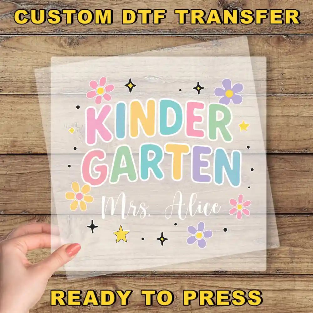 The image is a hand holding a transparent sheet with a colorful design and text, which appears to be a custom DTF transfer.