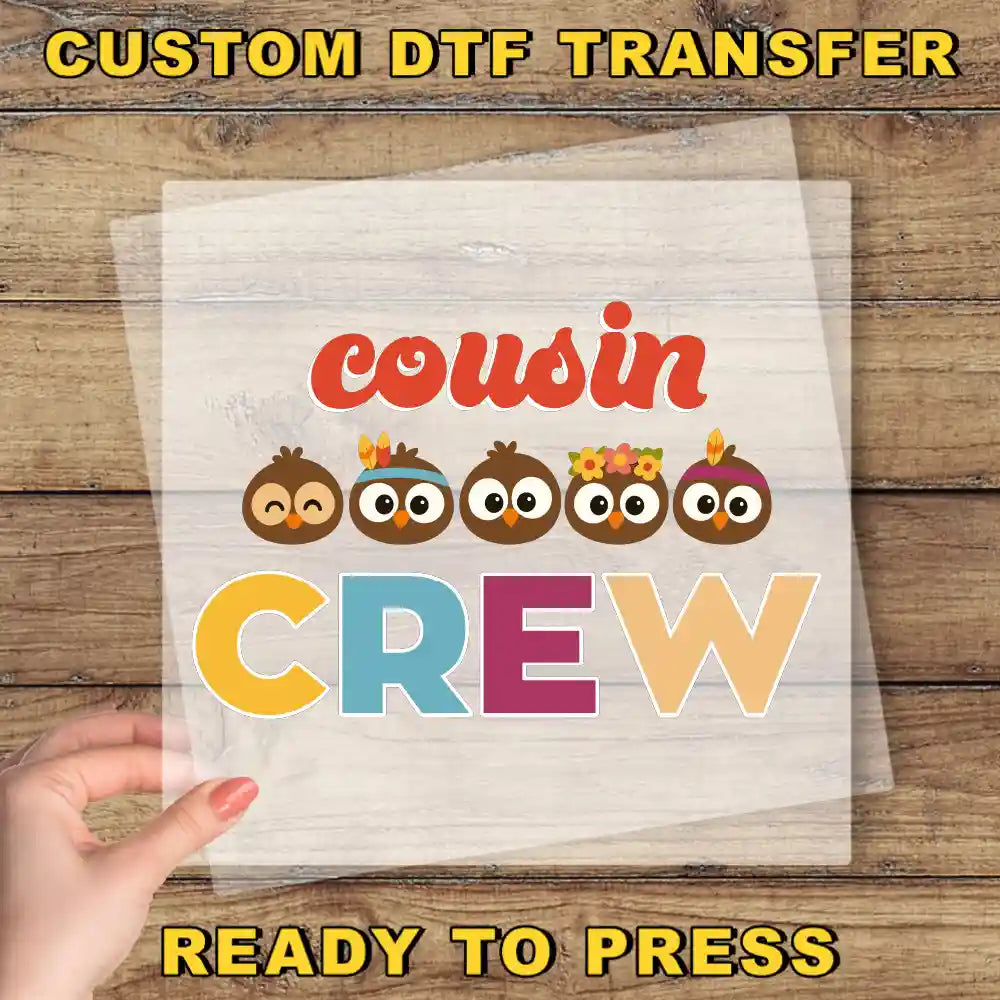 The image is a promotional poster for a custom DTF transfer service. It features a hand holding a clear sheet with the text "Cousin Crew" written on it, along with a group of cartoon owls wearing headbands. The background is a wooden surface.
