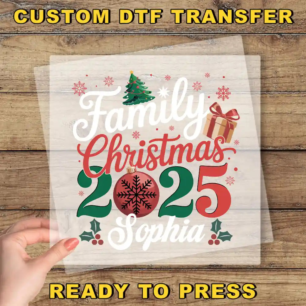 A hand is holding a transparent sheet with a festive Christmas design featuring text and decorative elements such as a tree, snowflakes, and a gift box.