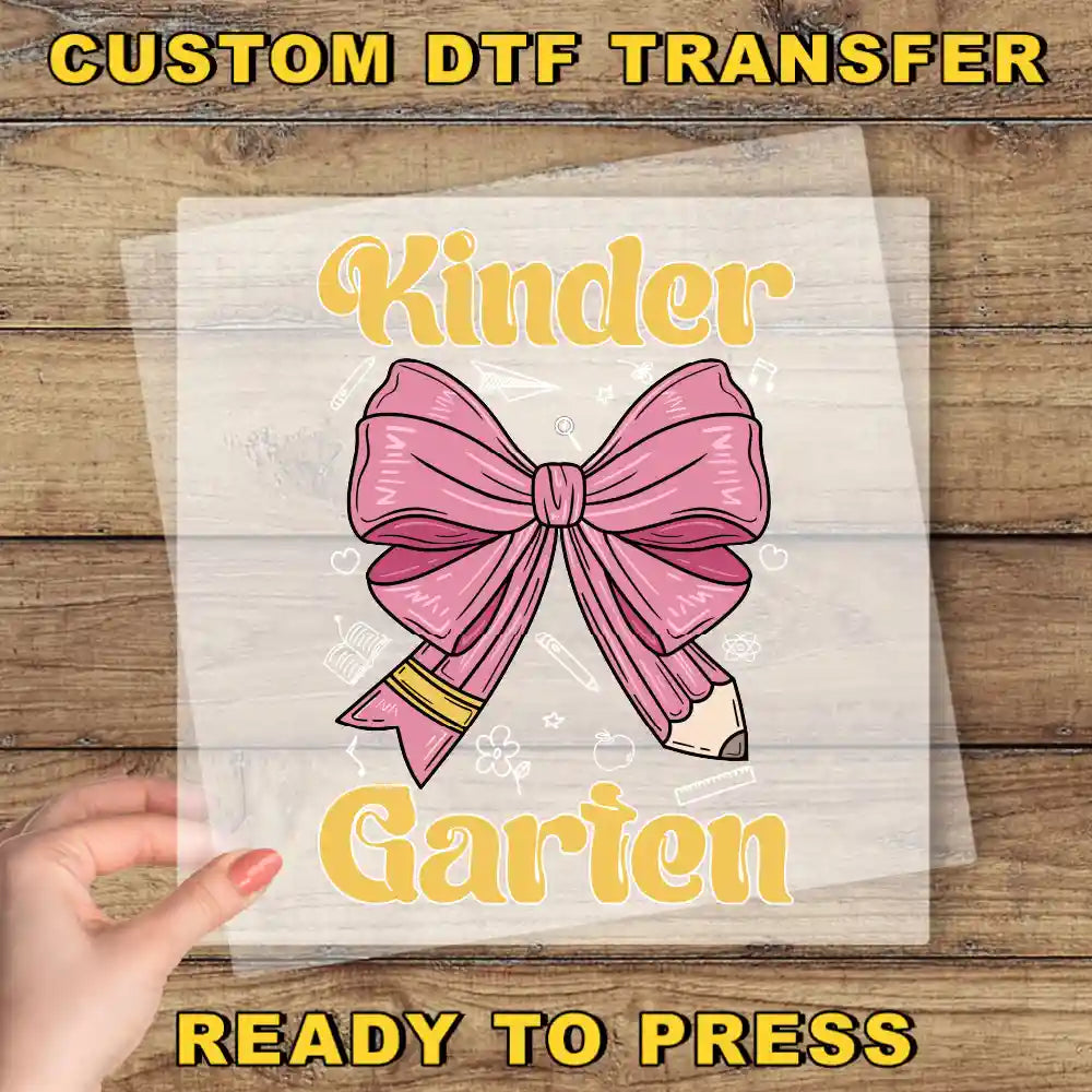 a hand holding a transparent sheet with a pink bow and a pencil graphic, along with the text "Kinder Garden" and "Ready to Press" written on it.