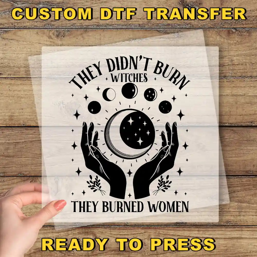 The image is a hand holding a transparent sheet with a graphic design featuring a crescent moon, stars, and the text "They didn't burn witches, they burned women".