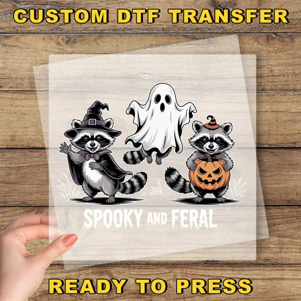 A hand is holding a clear sheet with a Halloween-themed illustration of a raccoon dressed as a witch and a ghost, along with a pumpkin.