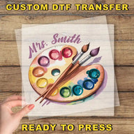 a person holding a piece of paper with paint and brushes on it