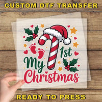 The image is a Christmas-themed graphic with a hand holding a transparent sheet that displays the text "My 1st Christmas" surrounded by festive elements such as a candy cane, holly leaves, and stars.