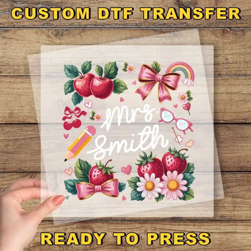 The image is a hand holding a transparent sheet with a colorful illustration of various objects, including apples, flowers, and a pencil, along with the text "Mrs. Smith" written on it.