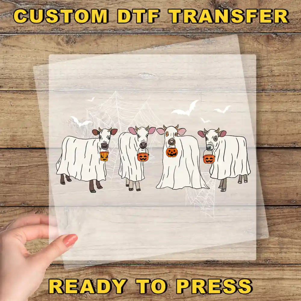 a hand holding a transparent sheet with a Halloween-themed illustration of cows dressed in ghost costumes, holding pumpkins.