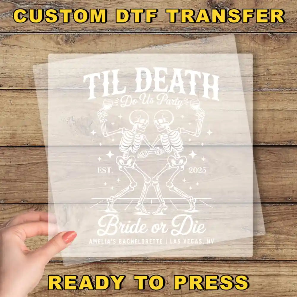 The image is a promotional poster for a custom DTF transfer service. It features a skeleton design with the text "Til Death Do Us Party" and "Amelia's Bachelorette Las Vegas, NV" printed on it. The poster is placed on a wooden surface, and there is a hand holding it up, suggesting that the viewer is ready to press the transfer button.