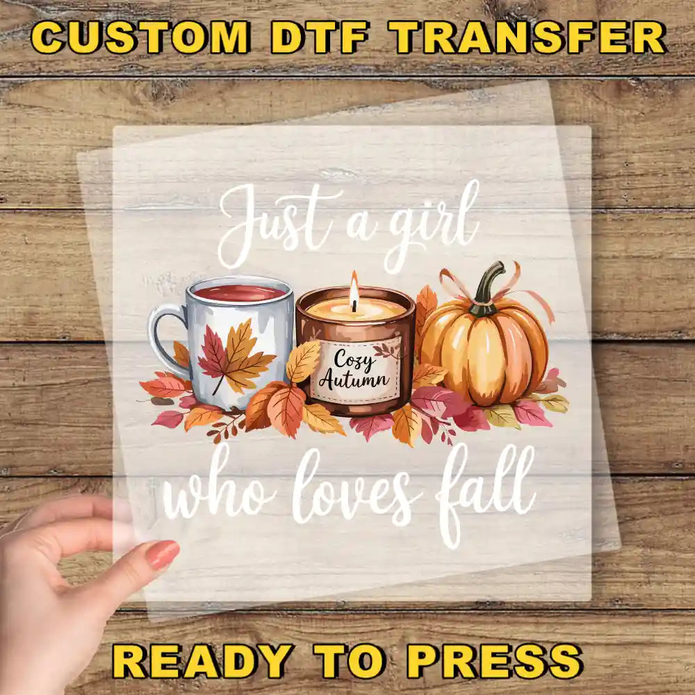 A hand is holding a transparent sheet with a design featuring a candle, a mug, and a pumpkin surrounded by autumn leaves.