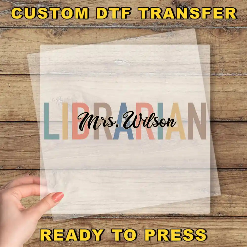 a hand holding a clear sheet with the word "LIBRARIAN" written on it, placed on a wooden surface.