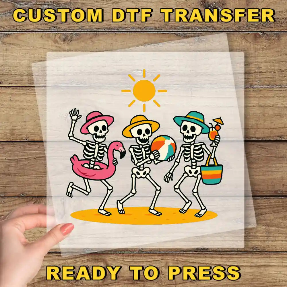 A hand is holding a transparent sheet with a cartoon illustration of three skeletons dressed in summer attire, including a pink flamingo, a beach ball, and a beach bag, against a wooden background.