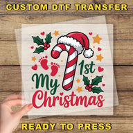 The image is a hand holding a clear sheet with a Christmas-themed design, including a candy cane, holly leaves, and a baby's foot.