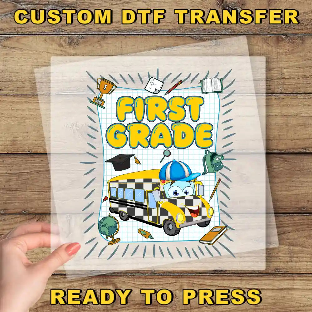 The image is a hand holding a clear sheet with a cartoon image of a school bus and various school supplies, including a globe, a trophy, and a book, along with the text "FIRST GRADE" and "READY TO PRESS".