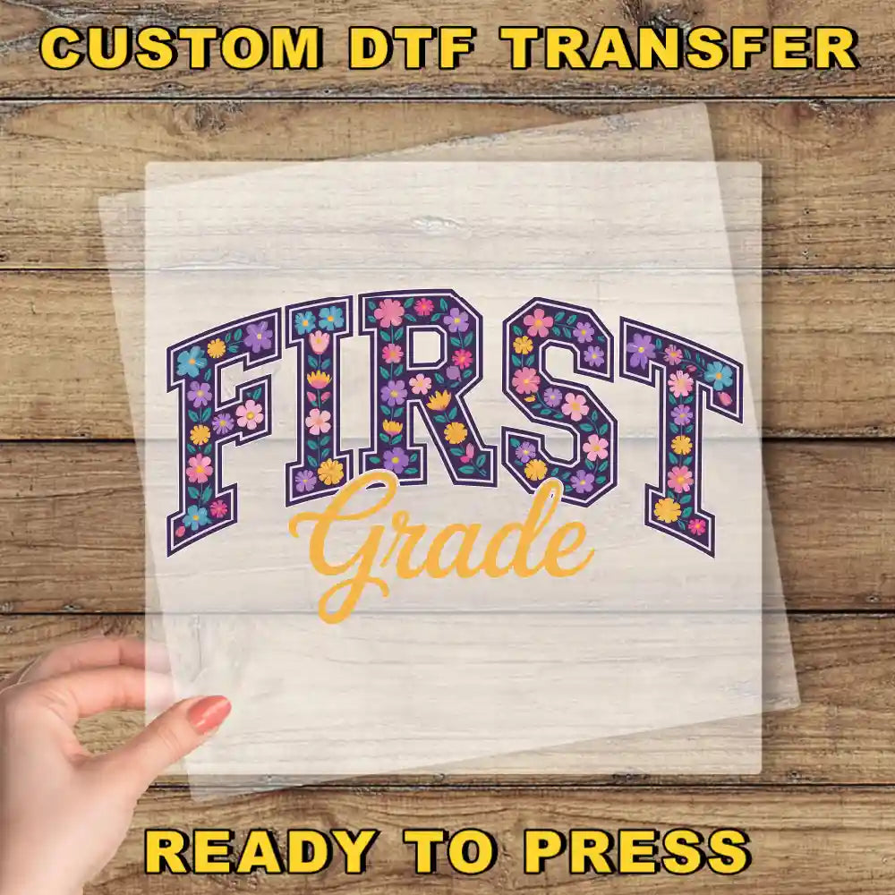 a hand holding a piece of paper with the text "FIRST Grade" printed on it, along with a "Custom Dtf Transfer" label.