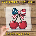 a hand holding a piece of paper with a bow and two cherries on it