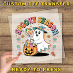 A hand is holding a clear sheet with a Halloween-themed graphic design featuring a ghost character holding a basket of candy and a jack-o-lantern.