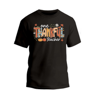 A black t-shirt with a colorful graphic design that says "One Thankful Teacher" in a stylized font.