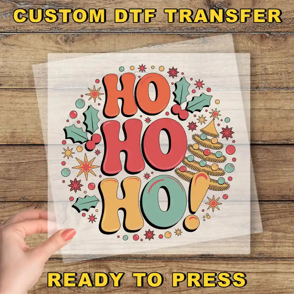 A hand is holding a clear sheet with a colorful, festive design featuring the text "HO HO HO!" surrounded by various holiday-themed elements such as stars, holly leaves, and a Christmas tree.