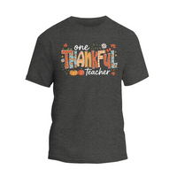 A gray t-shirt with a graphic design featuring the text "One Thankful Teacher" surrounded by autumn-themed elements such as leaves, pumpkins, and flowers.