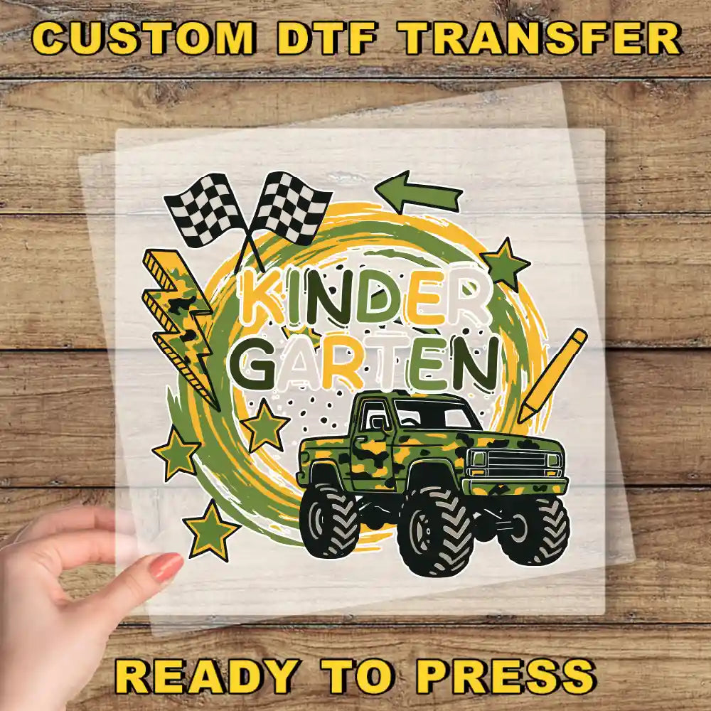 a hand holding a clear sheet with a colorful and playful design, including a truck, checkered flags, and stars. The text "KINDER GARTEN" is prominently displayed, suggesting this is a custom DTF transfer for a Kindergarten theme.