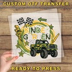 a hand holding a clear sheet with a colorful and playful design, including a truck, checkered flags, and stars. The text "KINDER GARTEN" is prominently displayed, suggesting this is a custom DTF transfer for a Kindergarten theme.