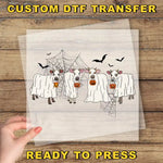 a hand holding a transparent sheet with a Halloween-themed illustration of cows dressed in ghost costumes, with bats flying around them.