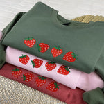 a pile of different colored shirts with strawberries on them