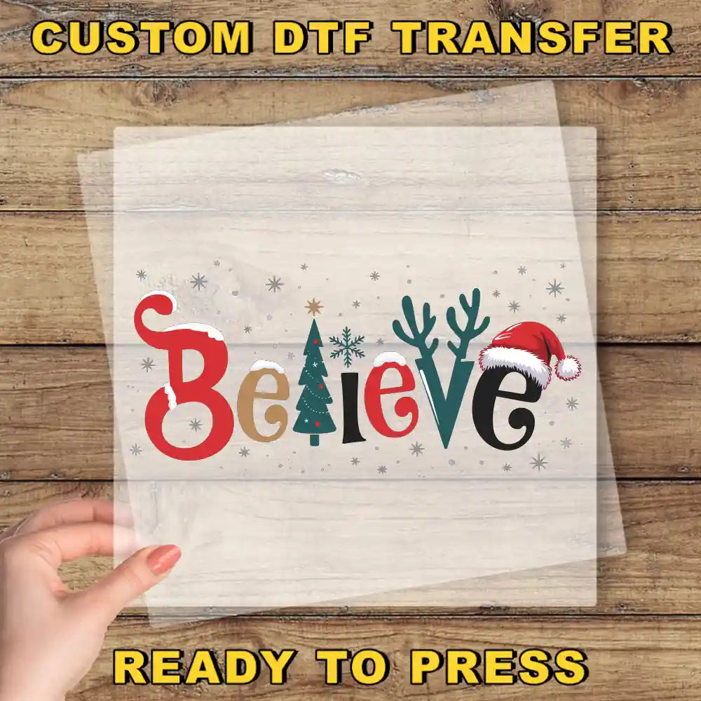 A hand is holding a clear sheet with the word "Believe" written on it, along with various Christmas-themed elements such as a snowman, reindeer, and a Santa hat.