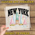 A hand holding a transparent sheet with a colorful illustration of New York City, including the Statue of Liberty, Christmas trees, and taxis.