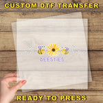 A hand is holding a transparent sheet with a design featuring a yellow flower and two bees, along with the text "beesites" written below the flower.