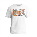 A white t-shirt with a graphic design featuring the text "One Thankful Teacher" surrounded by autumn-themed elements such as leaves, pumpkins, and flowers.