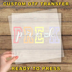 The image is a promotional image for a custom DTF (Digital Transfer Factory) transfer service. It features a hand holding a clear sheet with the word "PREK" printed on it, along with the text "CUSTOM DTF TRANSFER" and "READY TO PRESS" at the bottom.