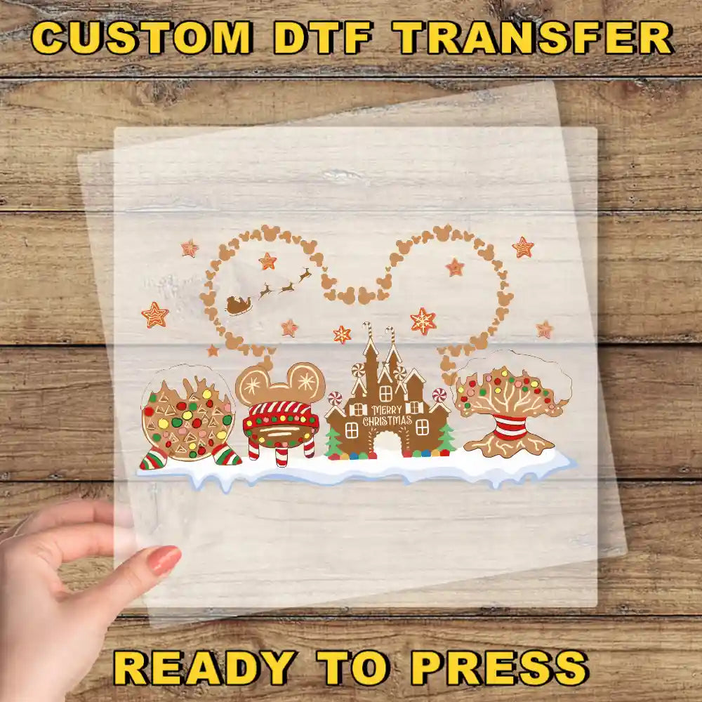 A hand is holding a clear sheet with a festive winter scene featuring various Disney-themed elements such as Mickey Mouse, a gingerbread house, and a snowman.