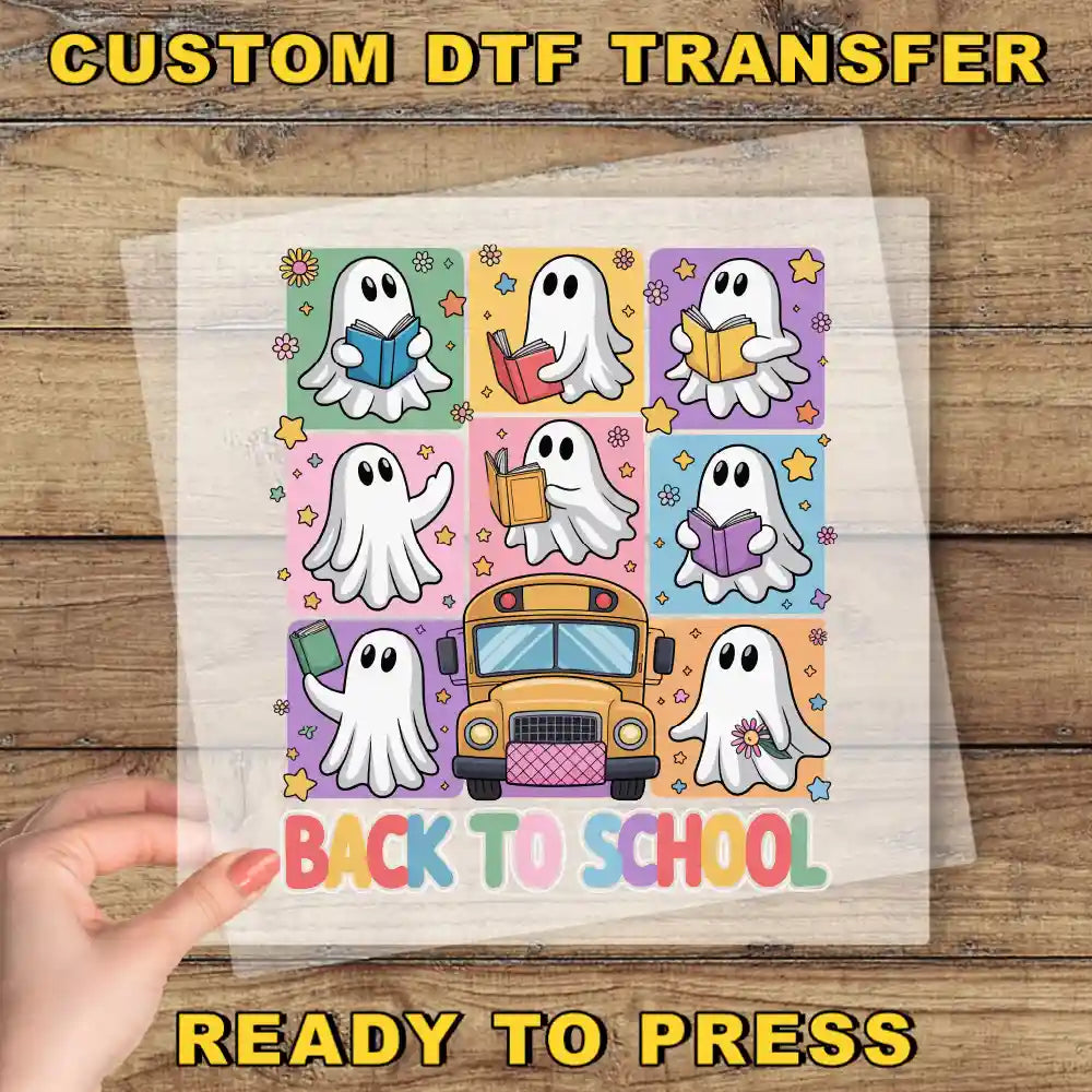 A hand is holding a transparent sheet with a colorful illustration of nine ghost characters, including a school bus, against a wooden background. The text "BACK TO SCHOOL" is displayed prominently in the center of the illustration.