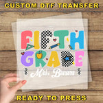 A hand is holding a transparent sheet with the text "Fifth Grade Mrs. Brown" printed on it, along with various colorful and playful illustrations.