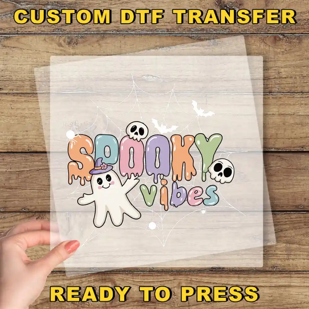 A hand is holding a transparent sheet with a colorful, spooky design featuring the text "SPOOKY VIBES" and a ghost character.