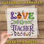 The image is a Halloween-themed graphic with the text "LOVE 1st Grade TEACHER" and various Halloween-related elements such as bats, pumpkins, and a spider web.
