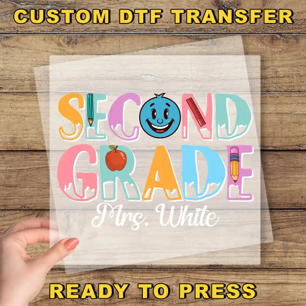 A hand holding a piece of paper with the text "Second Grade Mrs. White" printed on it, along with various school-related objects such as a pencil, apple, and ruler.