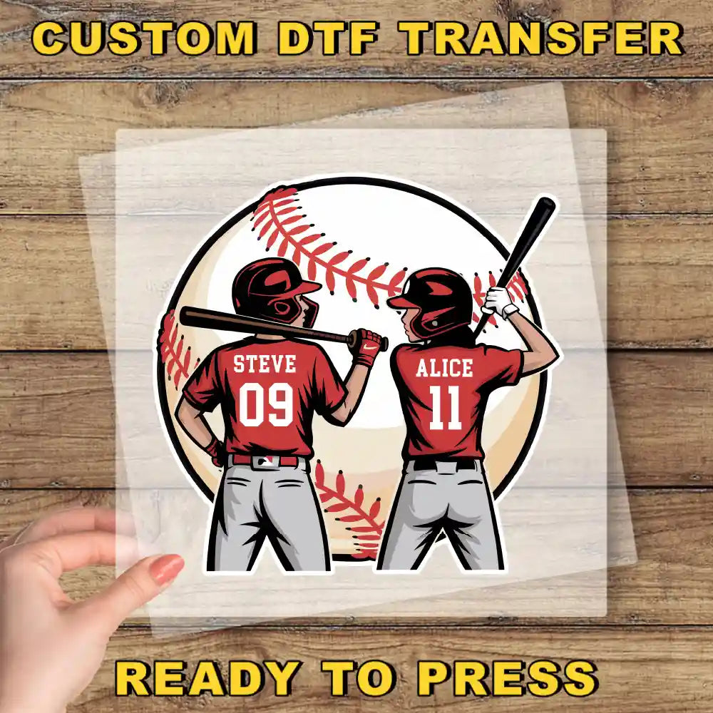 A hand is holding a clear plastic sheet with a cartoon illustration of two baseball players, Steve and Alice, standing in front of a baseball.