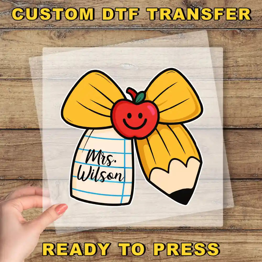 A hand is holding a clear sheet with a cartoon image of a pencil and a smiley face, along with the text "Mrs. Wilson" written on it.