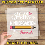 A hand holding a piece of paper with a pencil and the text "Hello Kindergarten I'm Hannah" printed on it.