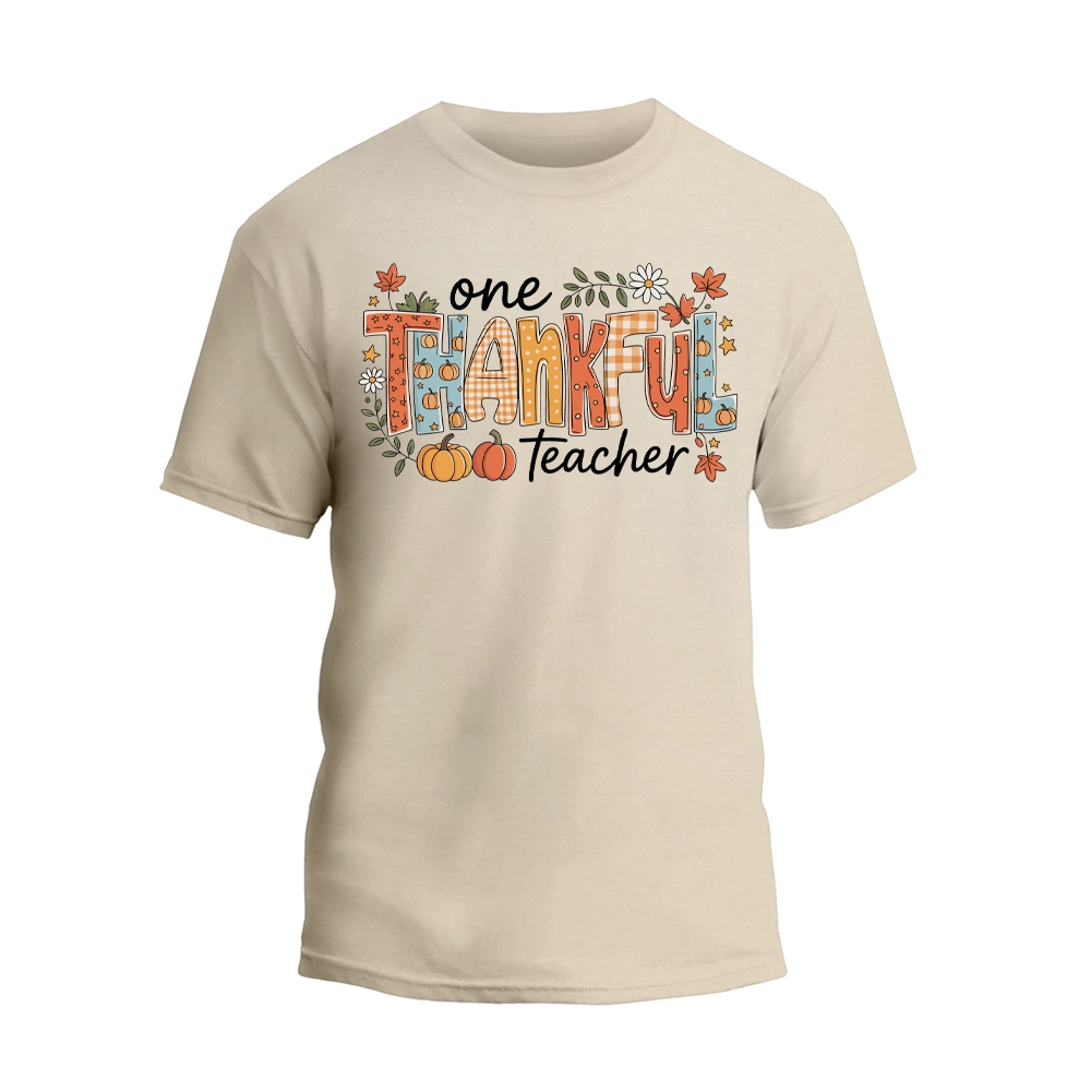 A beige t-shirt with a graphic design featuring the text "One Thankful Teacher" surrounded by autumn-themed elements such as leaves, pumpkins, and flowers.