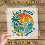 a hand holding a clear sheet with a vibrant, tropical-themed design on it. The design includes palm trees, a sun, and waves, conveying a sense of relaxation and enjoyment. The text "Salt Water and Sun Shine" is prominently displayed, suggesting a connection to the beach and the sun. The phrase "READY TO PRESS" is also visible, indicating that the image is ready to be printed or used.
